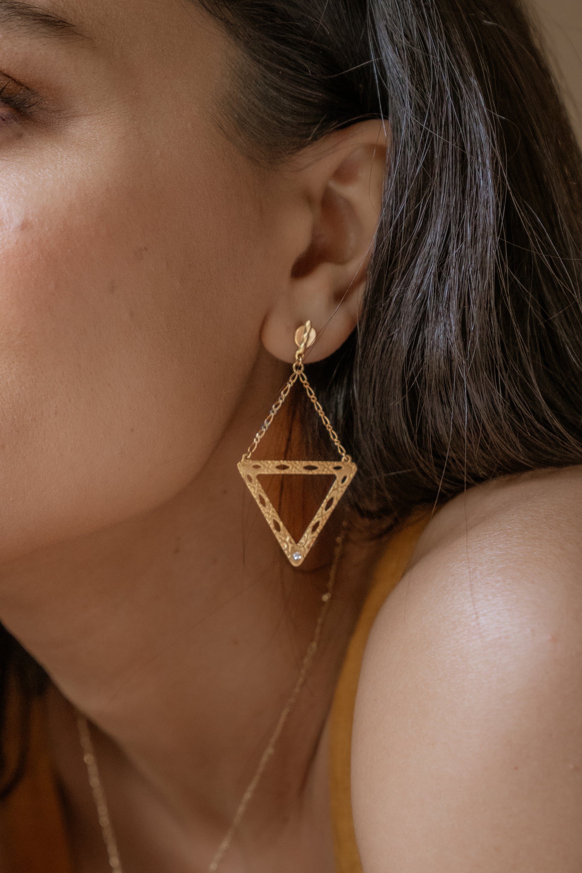 Like two souls finding their reflections in one another, the Tryst earring creates the illusion of mirrored triangles in a celebration of negative space. Dangling from a delicate chain, textured gold is dotted with open oblongs that draw the eye to the nadir of the triangle, where a sparkling diamond punctuates with brilliance.