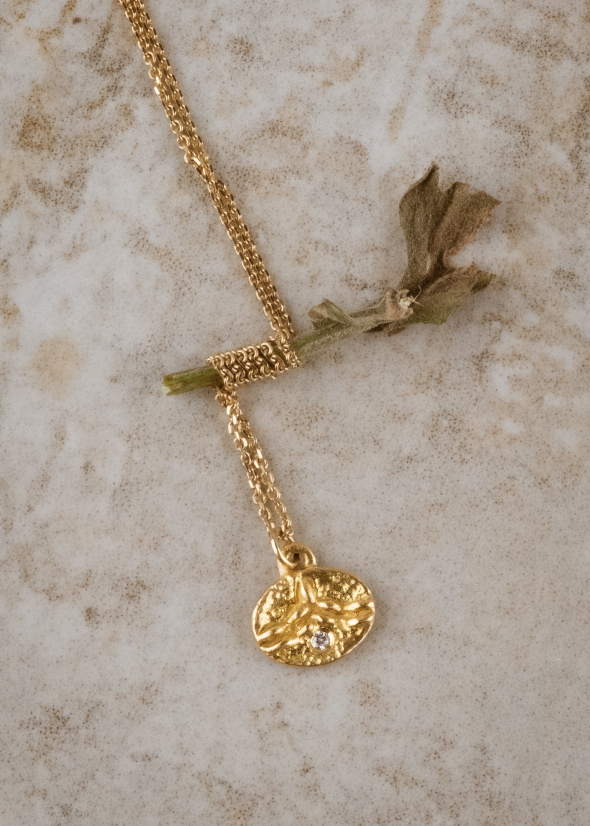 Inspired by the tiny beads of dew that cling to blades of grass on an early summer morning, the Dew necklace is hand-carved to reveal intricate texture and pattern across its coin-shaped pendant. A brilliant diamond catches the light, evocative of a dew drop itself—reflecting and refracting the beauty which surrounds it.