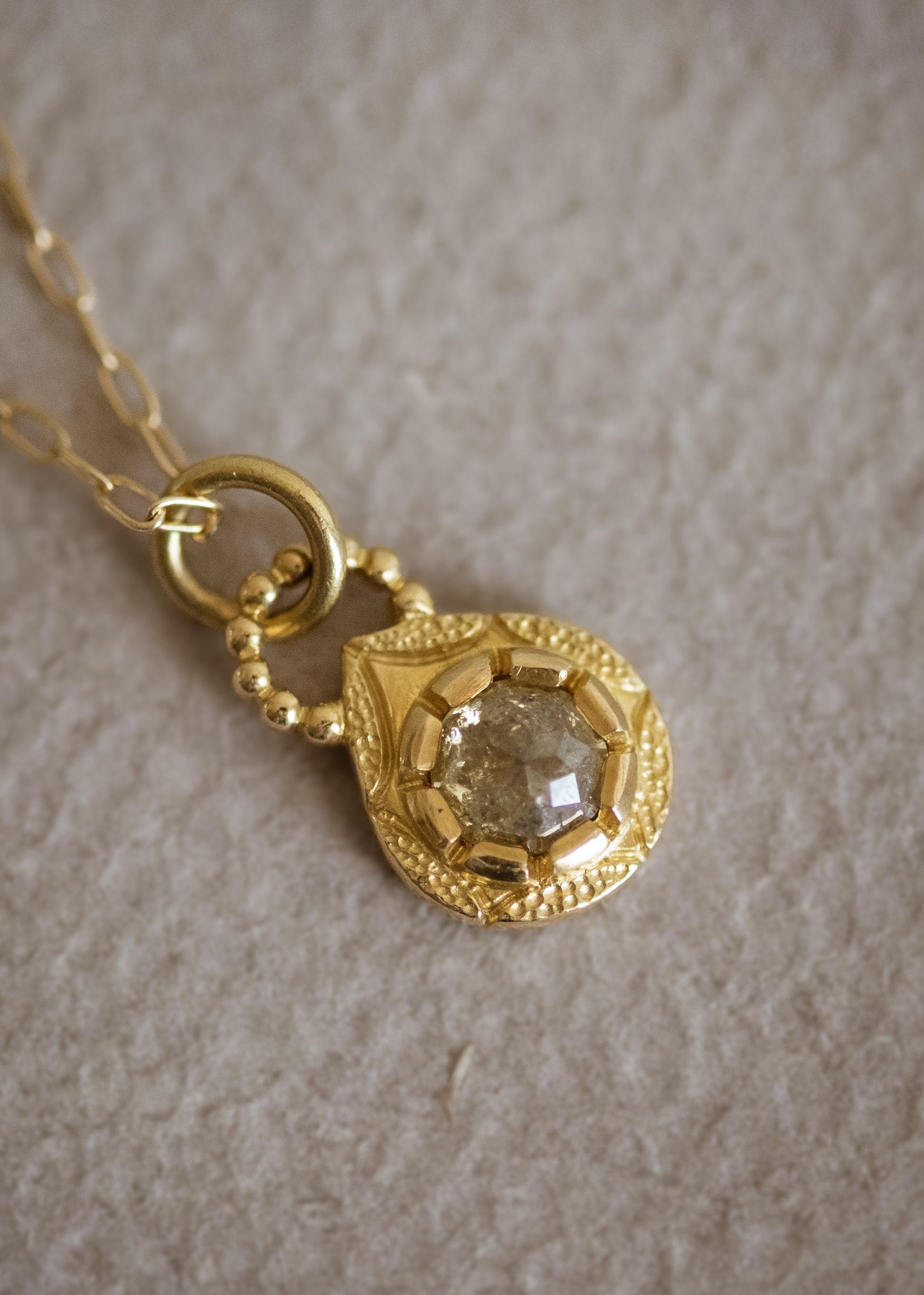 The Solo necklace revels in its unencumbered beauty. A stunning rose cut diamond is cradled in a gold droplet, revealing delicate texture and detail. An intricate beaded arch balances the pendant, linking it to its chain while showcasing its ornate character.