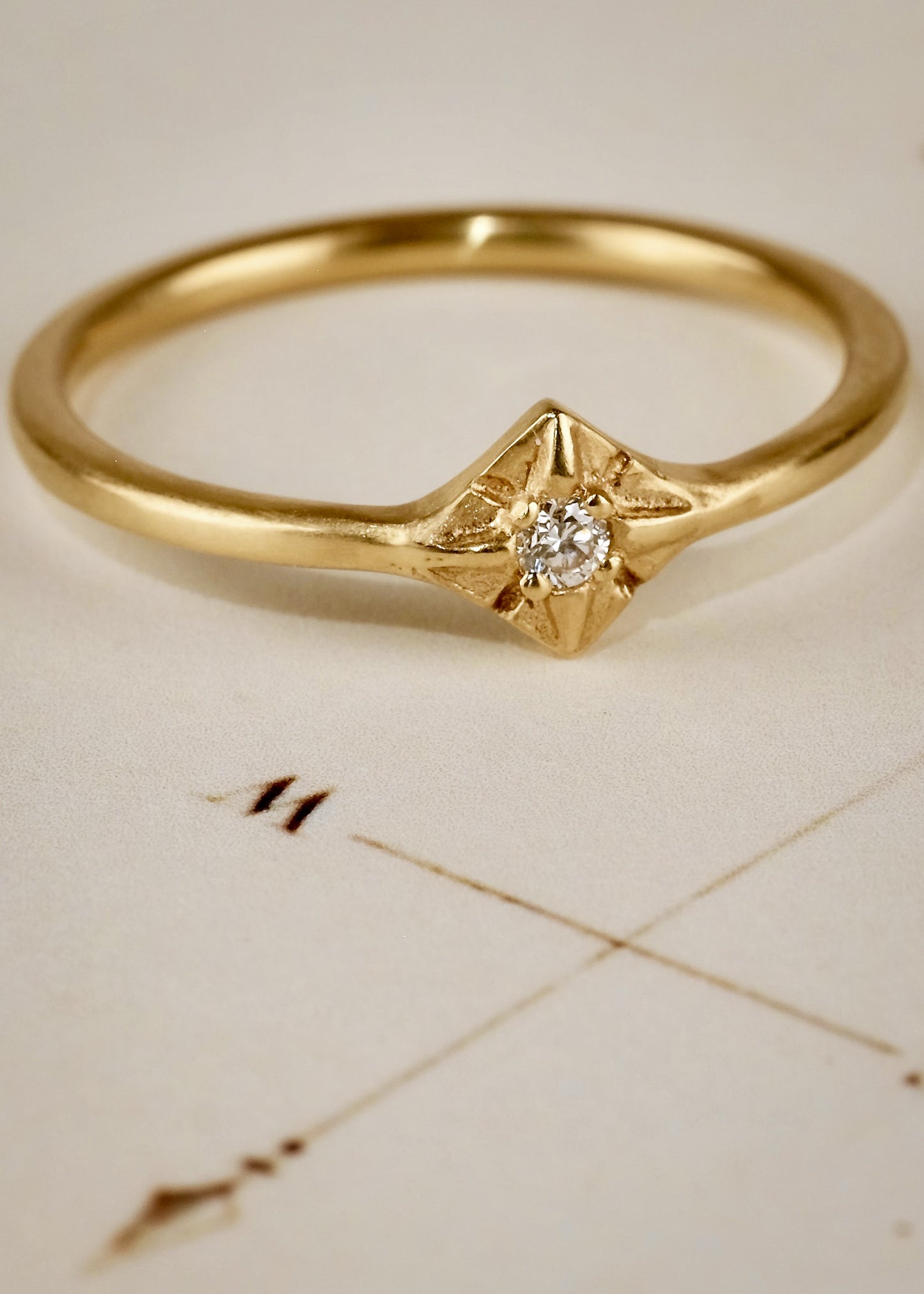 Through the sharp peak of a dormer window, a single star catches the eye: At the apex of the constellation it shines, as if hung by the starmaiden Astrea herself. Named for the Greek goddess, the Astrea ring features an understated band that encircles the finger to give way to a brilliant diamond that nestles between the zenith and nadir of a golden horizon. Hand-carved detail surrounding the diamond enhances its brilliance.