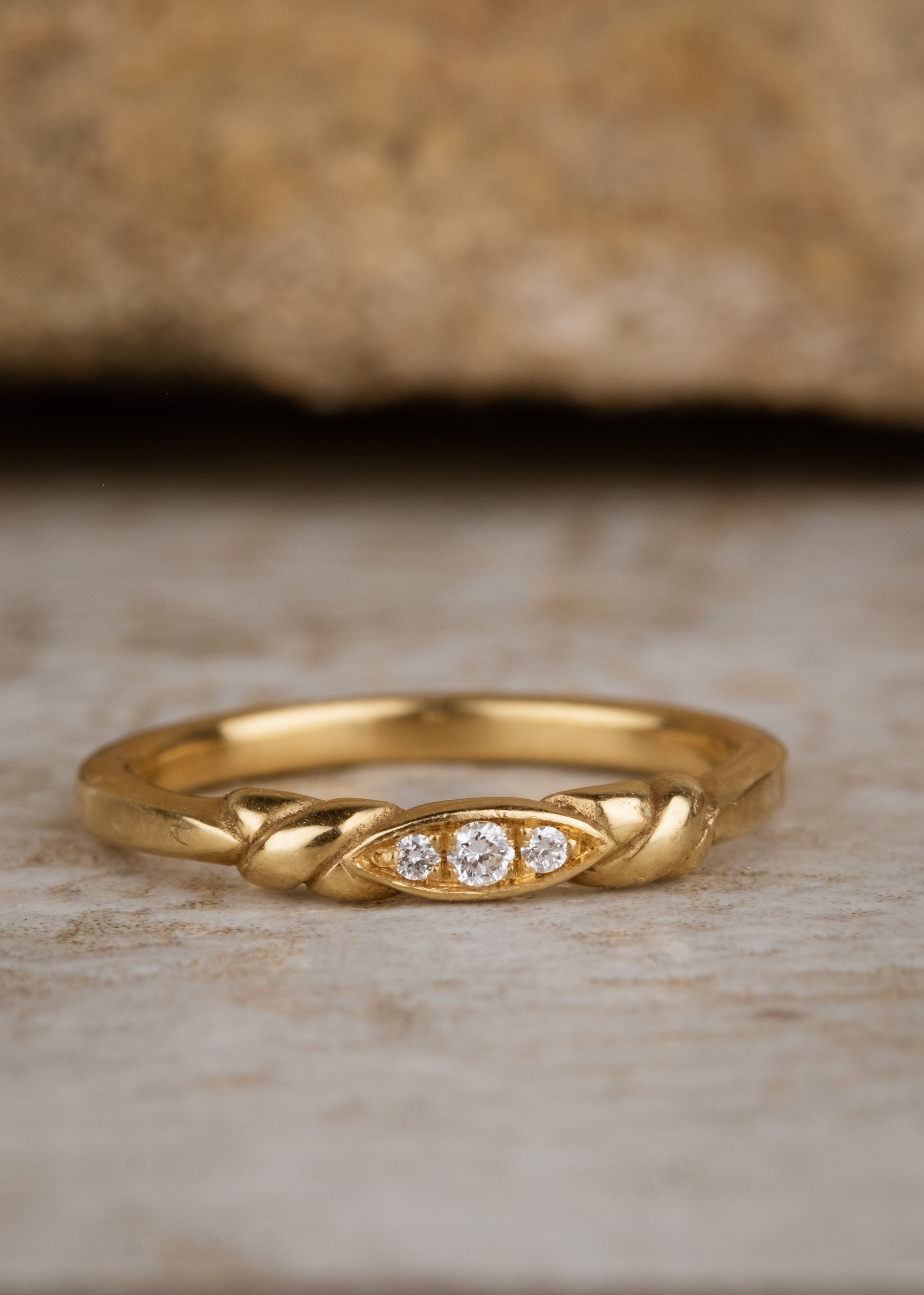 An engagement ring re-imagined, the Kiat ring was inspired by a proposal among sun-soaked cattails and waves lapping the shores of a hidden inlet. A gold band criss-crosses on either side of a trio of diamonds—a piece imbued with promise.