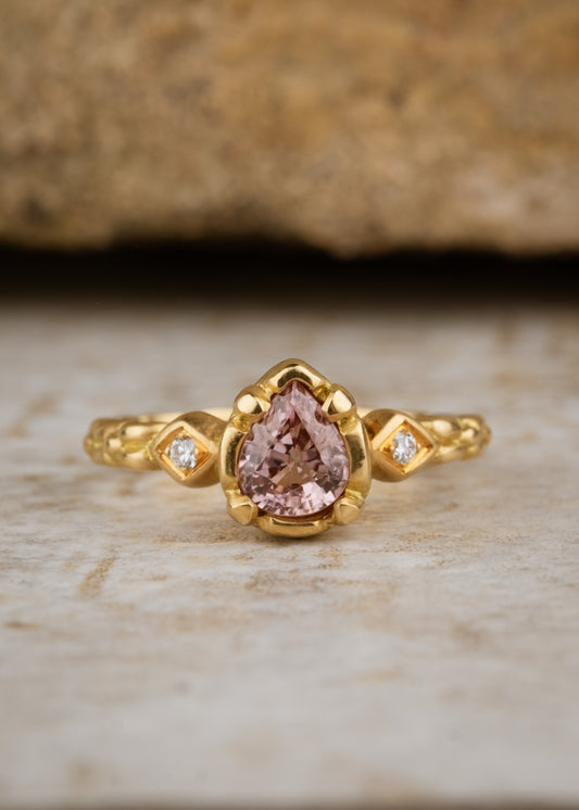 Stately and elegant, the Majestic ring is rich in exquisitely carved gold detail along the band, securing a pear-shaped pink zircon that commands attention—a piece evocative of royalty. 