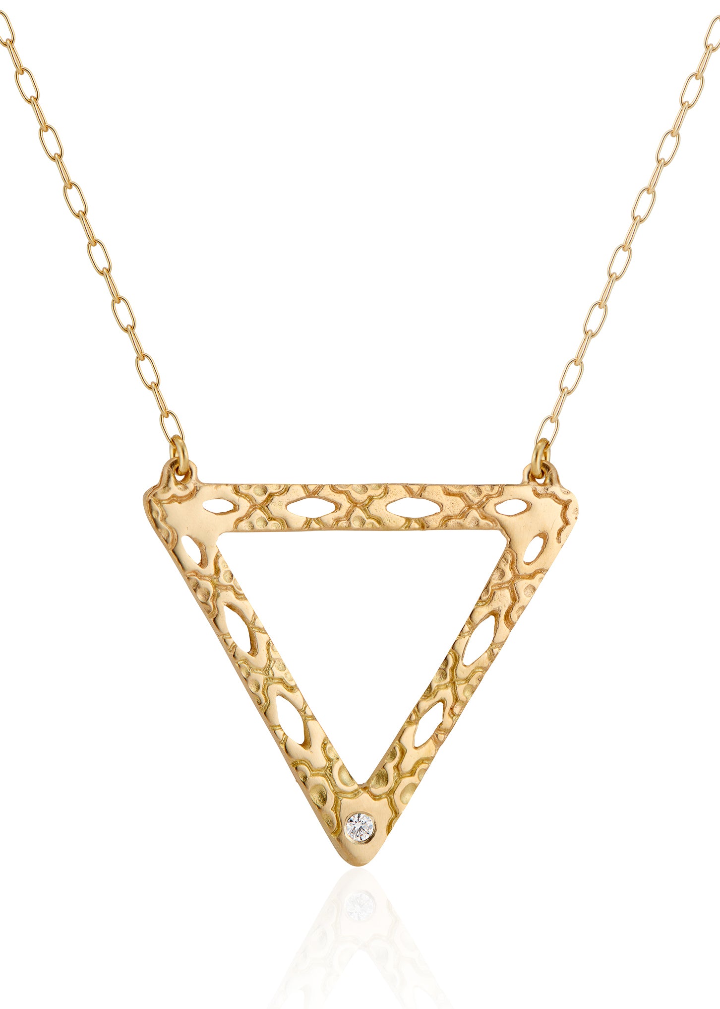 Like two souls finding their reflections in one another, the Tryst necklace creates the illusion of mirrored triangles in a celebration of negative space. Dangling from a delicate chain, hand-carved textured gold is dotted with open oblongs that draw the eye to the nadir of the triangle, where a sparkling diamond punctuates with brilliance. 